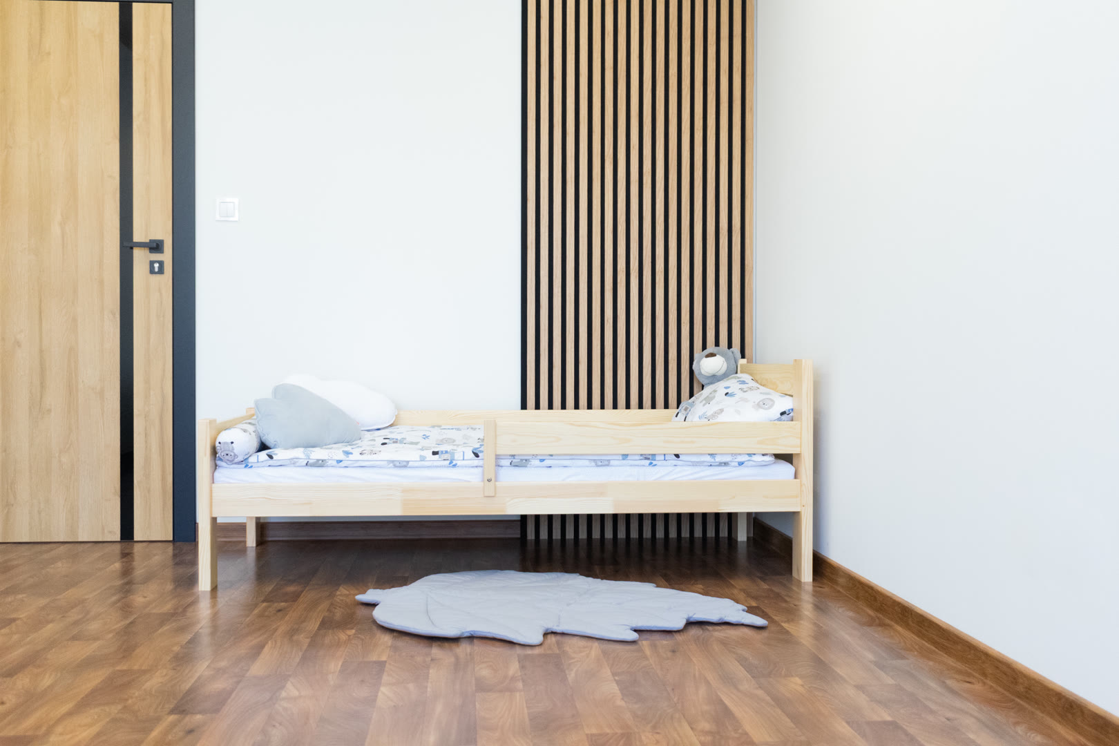 Niskie łóżko dziecięce z drewna sosnowego z pościelą w ciepłych kolorach w niewielkim pokoju